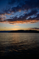 A mesmerizing sunset paints the sky with deep blue, orange, and red hues over Lake Ohrid, with a silhouetted town on the distant shore and calm water surface.