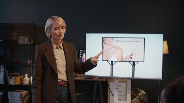 Elegant mature producer showing references of cosmetic products photo in studio while her colleagues listening to her