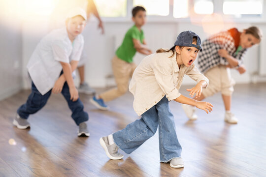 Emotional tween girl mastering krump dance routines during lively group session in children dance studio, guided by passionate male teacher..