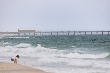 Gulf Shores Alabama Beach Scene With Intentionally Blurred Child Playing at Water's Edge and Pier in Background