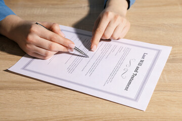 Woman signing Last Will and Testament at wooden table indoors, closeup