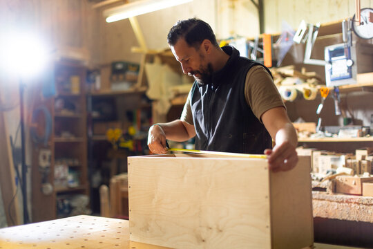 Carpenter measures wood for a custom storage box in workshop