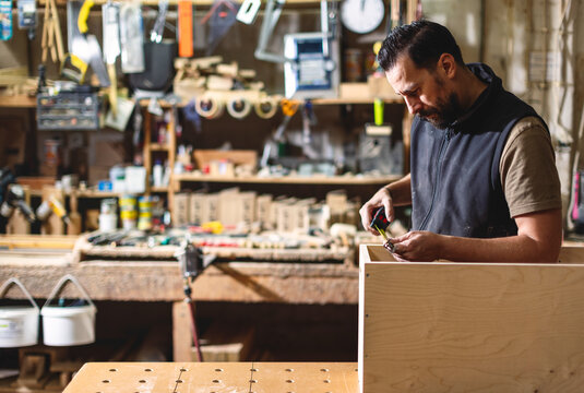 Woodworker measures wood for project in workshop during daylight
