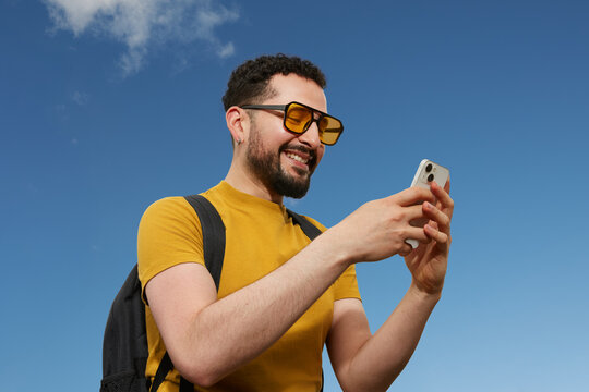 Young traveler using smartphone outdoors with blue sky background
