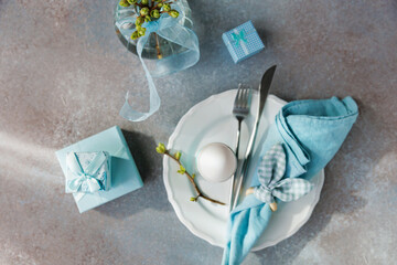 Flat lay of Easter table with egg, blue napkin, budding vase, and wrapped gifts