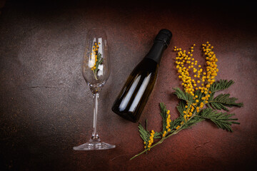 Glass with mimosa and champagne bottle on dark brown textured background