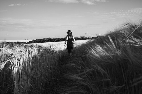 Dramatic black and white shot of a woman in a dark dress running through a tall grain field towards the horizon, symbolizing freedom, solitude, and artistic mystery