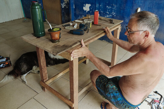 Senior carpenter working on a wooden table in his blue workshop