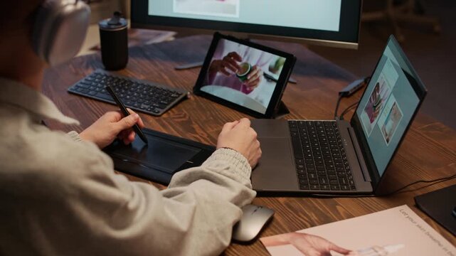 Unrecognizable man listening to music while sitting at desk and using interactive tablet to edit images