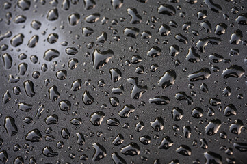 Macro shot of clear water droplets on a dark matte textured surface. Minimalist abstract background with liquid drops, bokeh and dramatic lighting. Close-up view