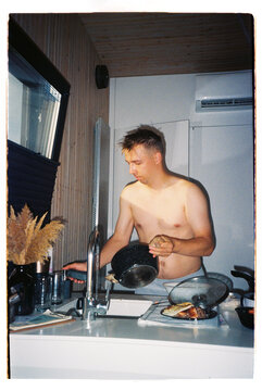 Man washing dishes in a small wooden kitchen, - film analog