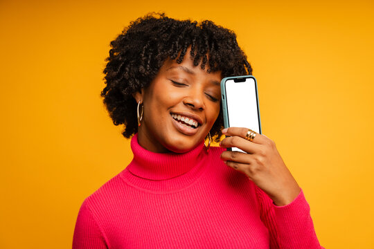 Woman smiles in a studio and holds a mobile phone with blank screen