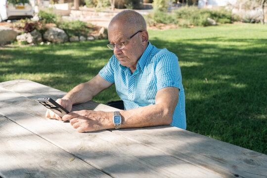 Elderly Man Reading on His Smartphone at a Park Table