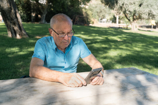 Elderly Man Using Smartphone for Mobile Payment in Sunny Park