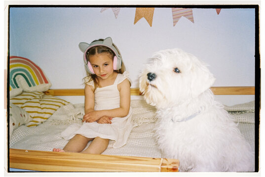 Film photo of little girl with headphones and white puppy at home