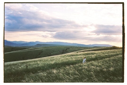 Film photo of little girl running across the big field with landscape 