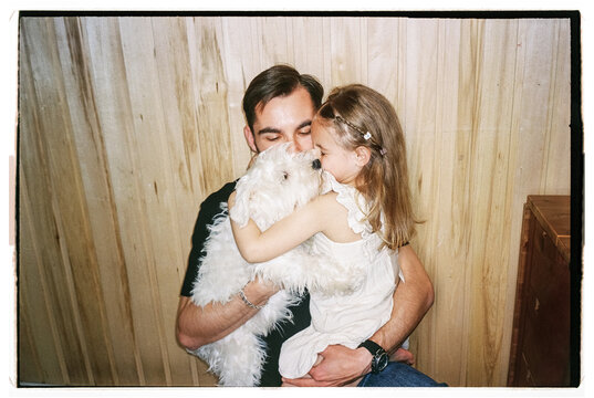 Film photo of happy dad, his daughter and their white puppy hugging 