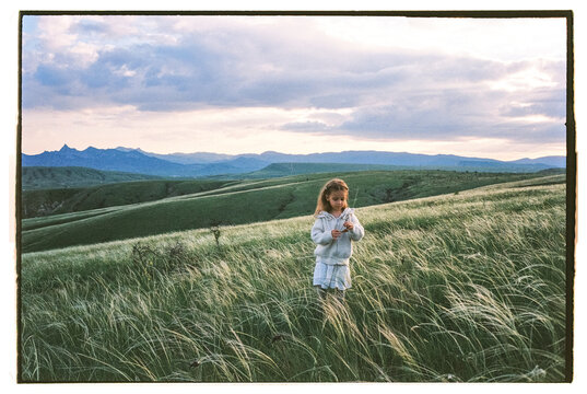 Film photo of little girl standing in the field with a mountains view 