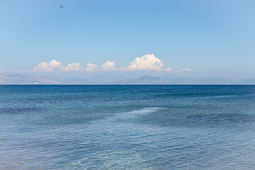 Crystal clear sea with white clouds on the horizon under blue summer sky