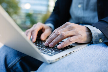Close-up of adult man typing on laptop outdoors. Focused professional working digitally in an urban...