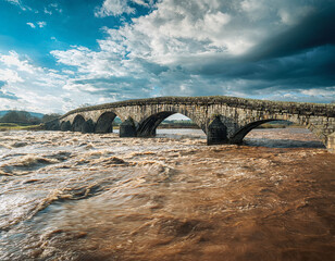 Stone bridge in storm and flood with swollen river