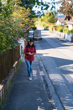 Woman Using Smartphone While Walking on Suburban Street