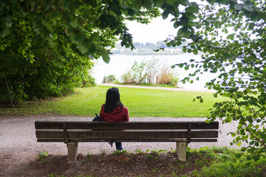 Woman Sitting on Park Bench Overlooking Tranquil Lake