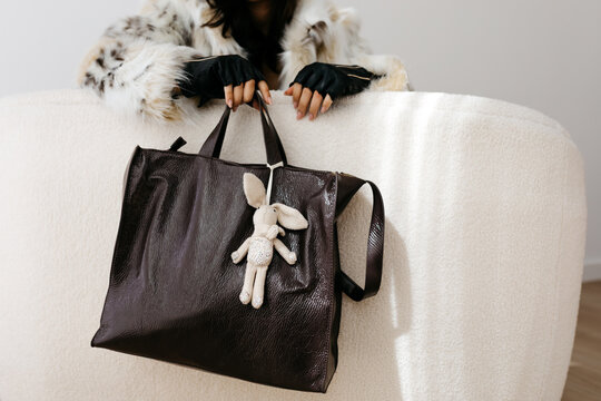 Woman holding dark leather bag with rabbit charm
