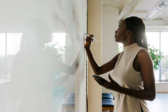 Woman writing on whiteboard during presentation at office