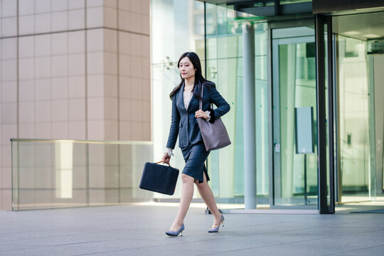Japanese business woman walking in city holding briefcase