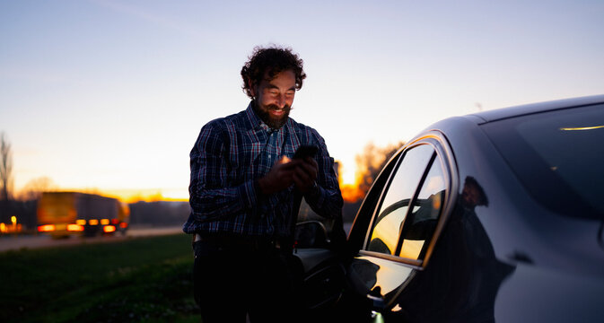 Smiling man checks his mobile phone while standing by a parked car