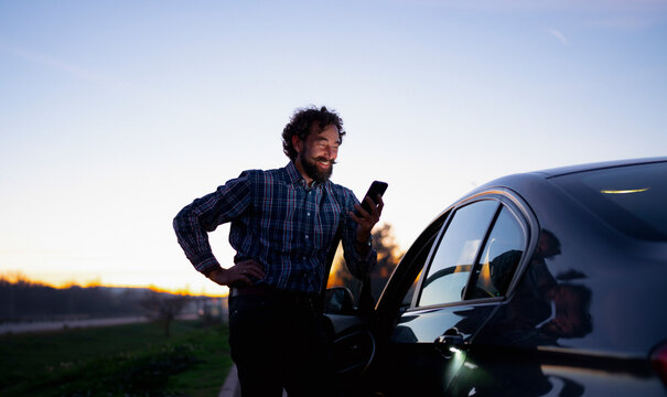Man in plaid shirt looks at smartphone while standing beside a car