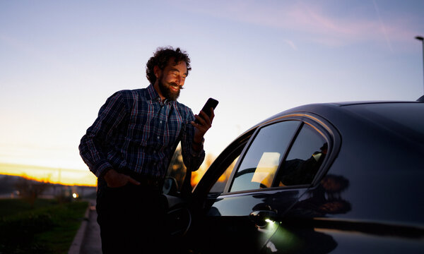Man smiling at smartphone near car during sunset in open area