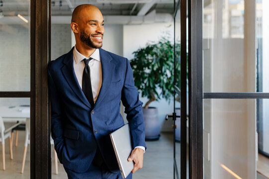 Confident businessman carrying laptop smiling in modern office