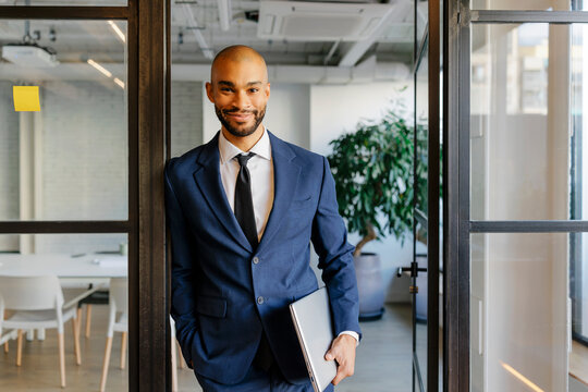 Confident businessman holding laptop while standing in modern office