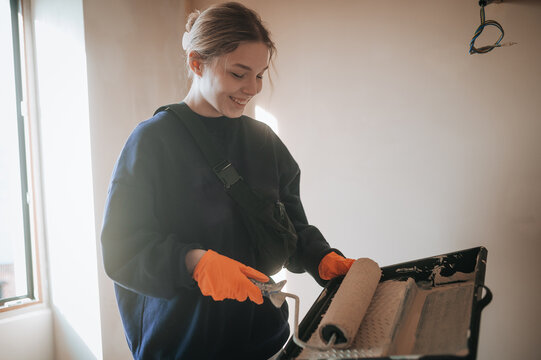 Young woman painting a room with a roller and tray
