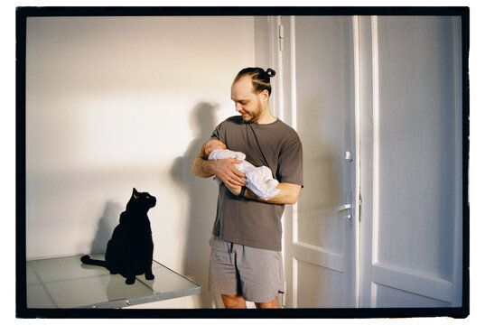 Father holding baby while cat observes quietly