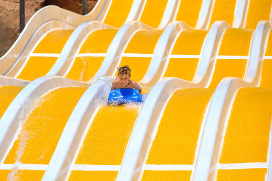Little boy sliding down yellow water park slide