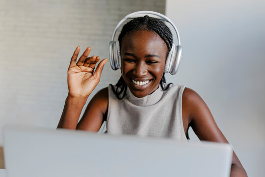 Smiling woman with headphones waving during video call