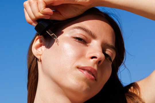 Skincare summer Woman Applies Facial Oil with Dropper blue sky