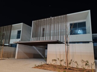 Two-story contemporary residences featuring cream-toned façades and sleek black-tinted glazing create a striking architectural presence.  Night View of Residential villa © Usama