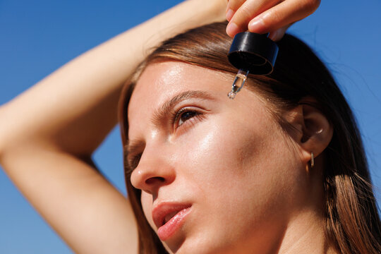 Woman Applying Facial Serum Under Bright Blue Sky Summer skincare 