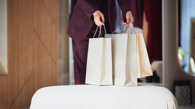 Closeup lady putting shoppings ottoman arrived store. Woman unpacking dresses