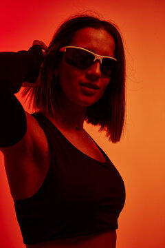 Stylish woman in sunglasses poses under vibrant orange lighting