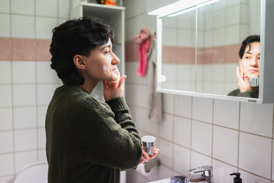 Person Applying Skincare Product in Bathroom Mirror Reflection