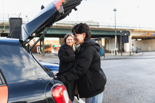 Happy Lesbian Couple Loading Luggage into Car Trunk