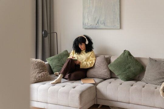 Woman relaxing on sofa with headphones and notebook