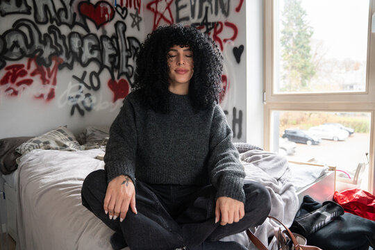 Young woman meditating in urban bedroom with graffiti