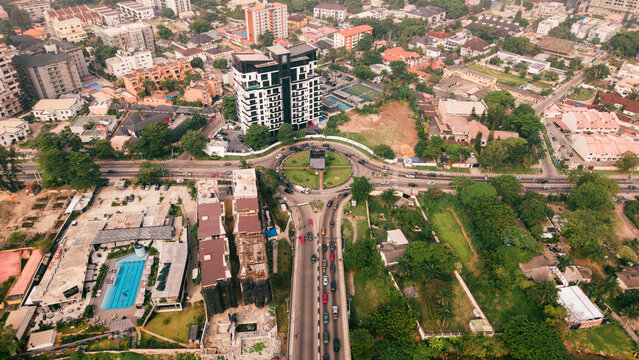 Aerial view of the vibrant roundabout, bordered by lush greenery and modern buildings, a symphony of urban life, Lagos, Nigeria.