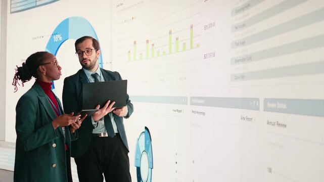 Female executive and business partner compile shareholder financial report using laptop in conference room. African american woman and coworker look at key performance indicators earnings data